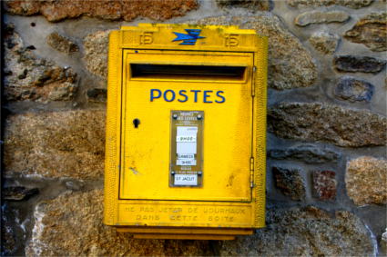 Ein alter gelber Briefkasten an einer Steinmauer.