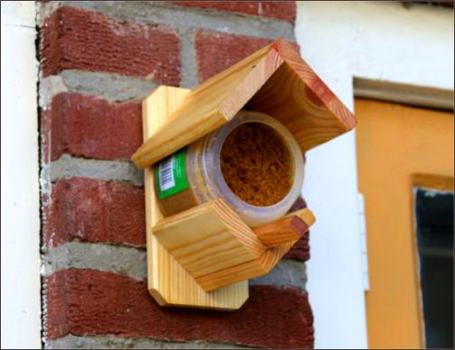 Ein kleiner Topf mit Fettfutter für Vögel in einer Haltekonstruktion an der Hauswand