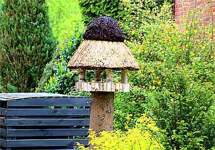 Ein Vogelhaus mit Reetdach auf einem abgesägten Stamm im Garten