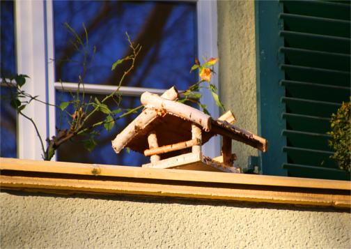 Ein kleines Vogelhaus aus Birkenholz steht auf der Balkonbrüstung